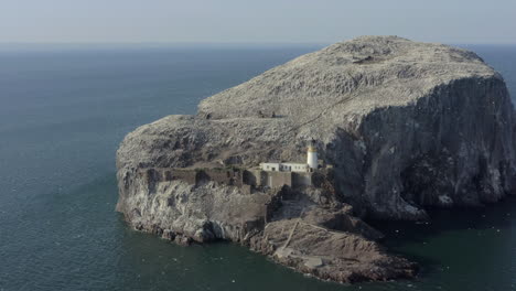 An-aerial-view-circling-Bass-Rock-and-lighthouse-as-gannet-seabirds-circle-their-island-colony-on-a-sunny-day,-East-Lothian,-Scotland