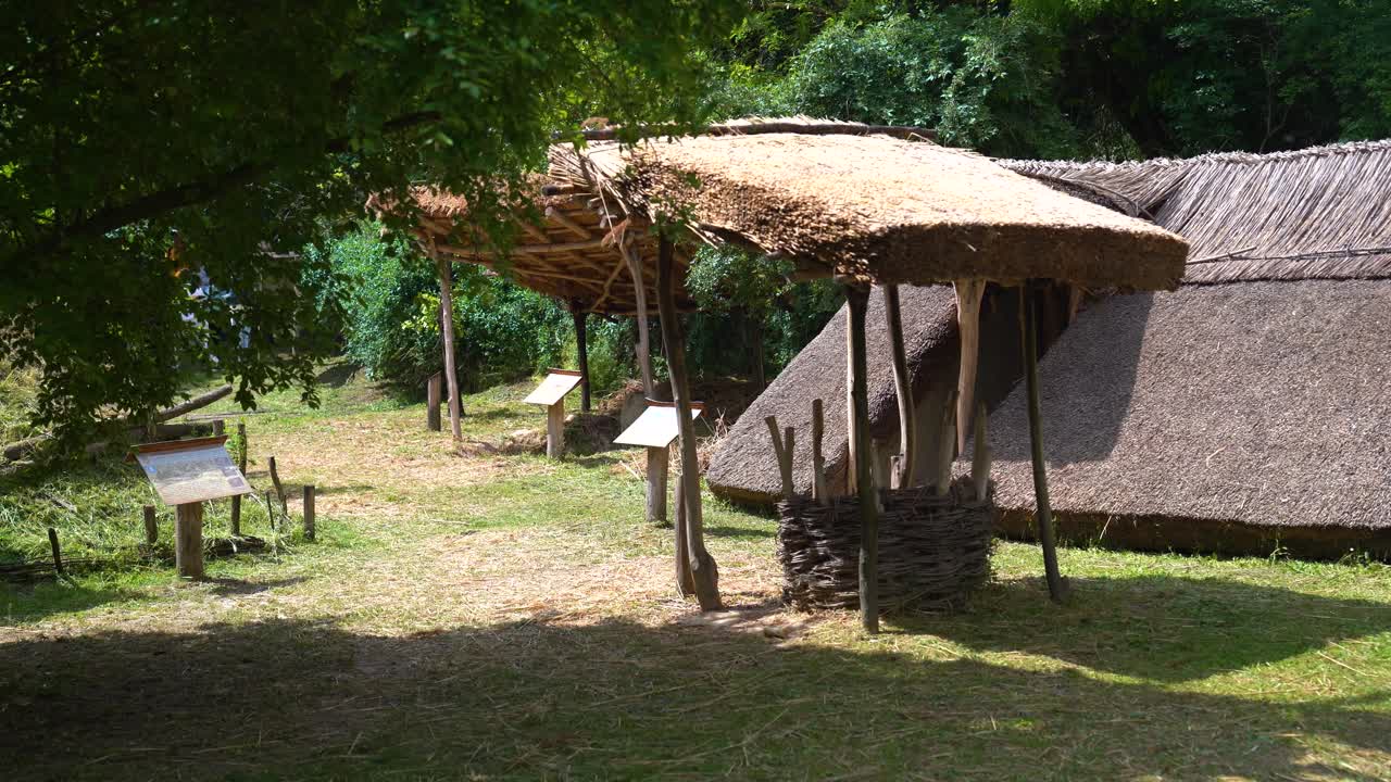 Thatched shelter structures in open-air museum village with wooden signage, Hungary