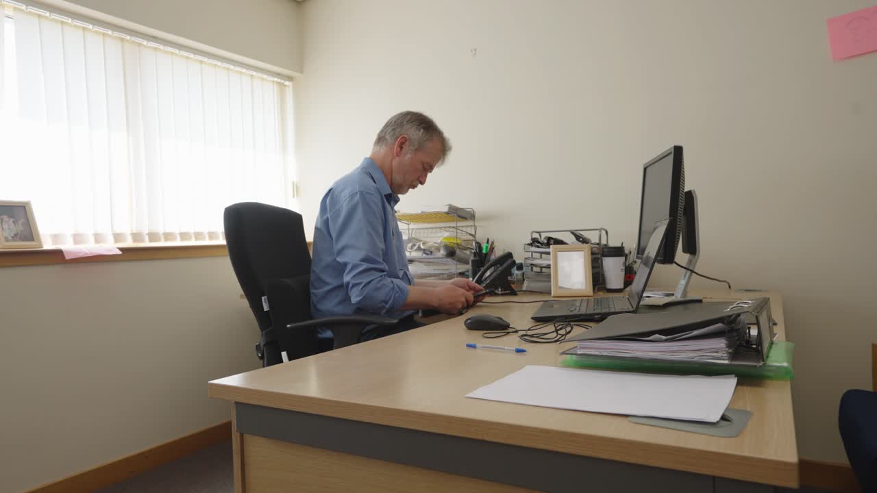 Sitting man in blue shirt using a smartphone in an office. locked off