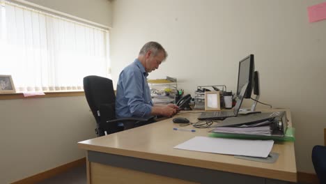 sitting man in blue shirt using a smartphone in an office. locked off