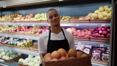 Young-man-in-apron-hold-basket-with-oranges-and-pose-on-camera