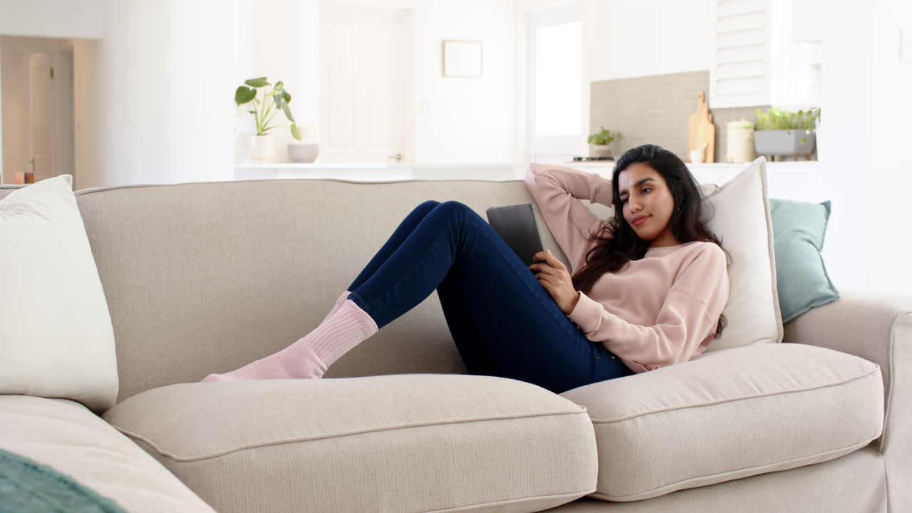 Relaxing at home, woman reading on tablet while lounging on sofa