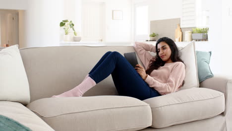 relaxing at home, woman reading on tablet while lounging on sofa