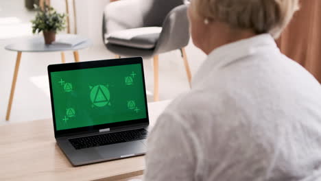 anciana sentada en un sofá en la sala de estar saludando y hablando por videollamada en una laptop moderna con pantalla verde