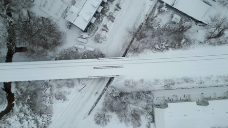 aerial top down overview of train tracks crossing above road passing homes in the winter snow