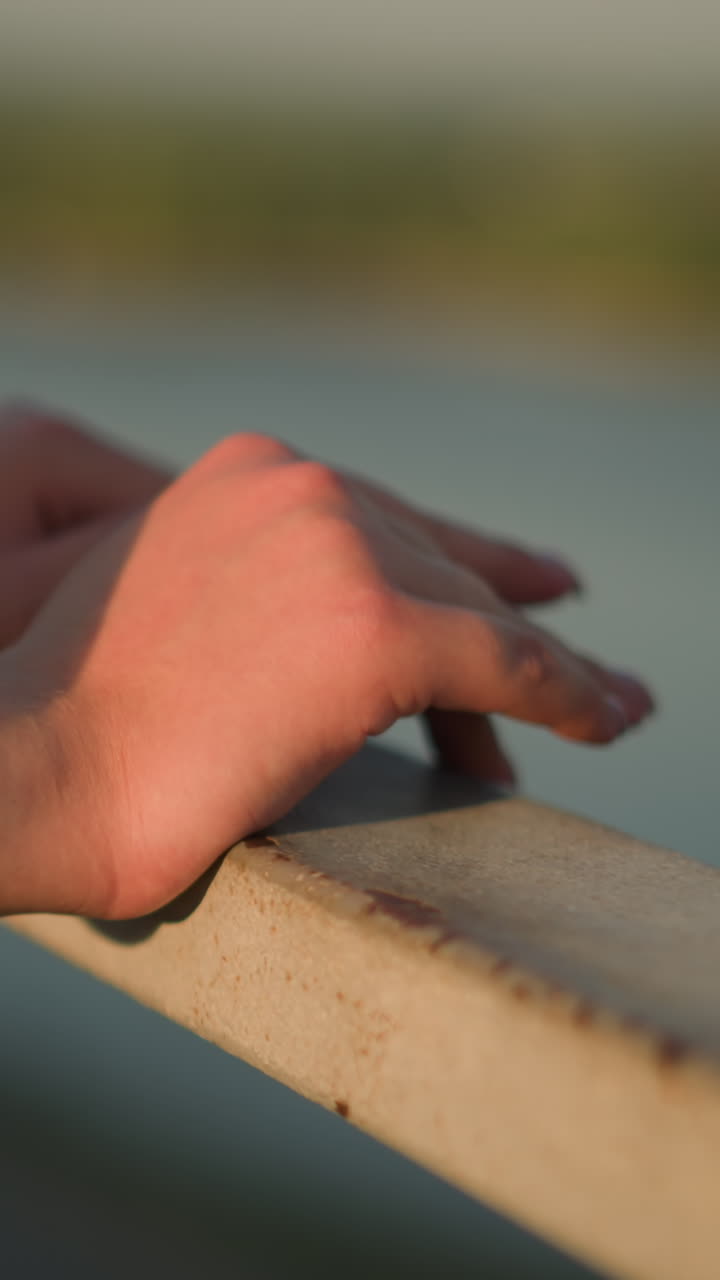 해가 지는 동안 철의 레일링에 손을 고 있는 백인 사람의 클로즈업, 손가락이 가게 만지고, 멀리 있는 초록색을 특징으로 하는 흐릿한 배경