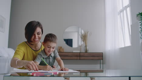 Beautiful-young-mother-in-a-warm-sweater-lying-on-the-floor-with-my-son-drawing-with-markers-on-paper-portraying-his-family.-The-child-learns-to-draw