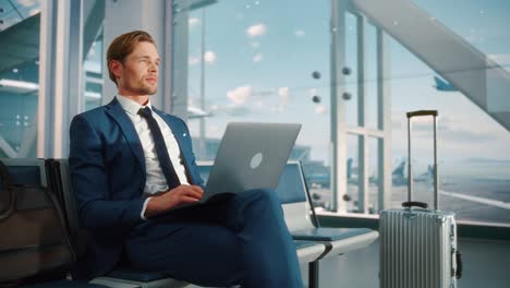 Airport Terminal: Businessman Uses Laptop Computer, Waiting for Flight to International Conference. Traveling Entrepreneur Remote Work Online Sitting in a Boarding Lounge of Airline Hub with Airplanes