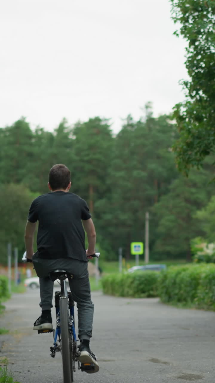 두 친구가 울창한 초록색 경로를 타고 자전거를 타고 있는 모습, 한 명이 서서 타고 다른 한 명이 앉아 있으며, 배경에는 멀리 있는 자동차의 흐릿한 시야가 있는 초록색이 있습니다.
