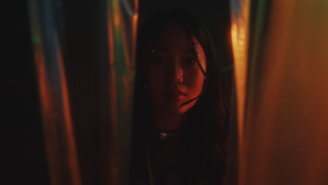 portrait of enigmatic asian woman behind cellophane curtains in neon light