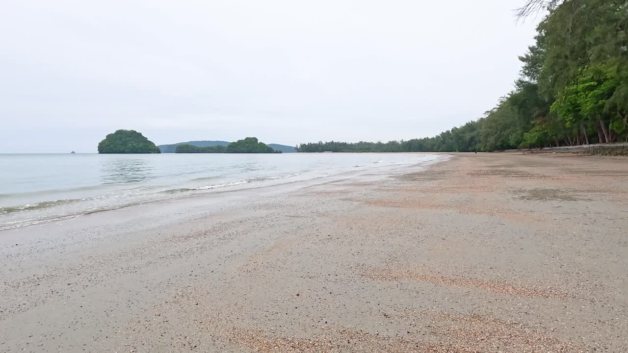 태국 크라비의 조용한 해변 장면, 부드러운 파도와 부드러운 자연 조명 아래 울창한 초록색을 보여줍니다.