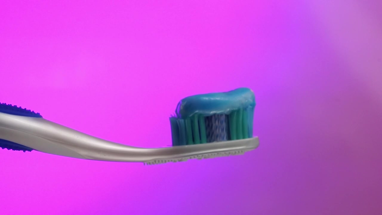 Close-up of a toothbrush with toothpaste on its blue bristles, with a purple blurred background