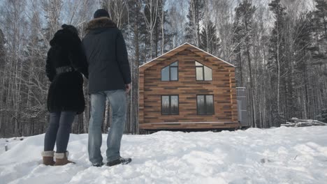 una pareja viendo una nueva cabaña de madera en el bosque nevado