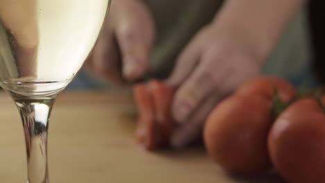 hands chopping fresh vine tomatoes with glass of white wine foreground