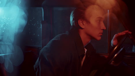 young melancholic man sitting in car at night, looking around