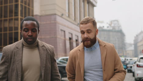 hombre de negocios caucásico y afroamericano con ropa elegante hablando y caminando por la calle