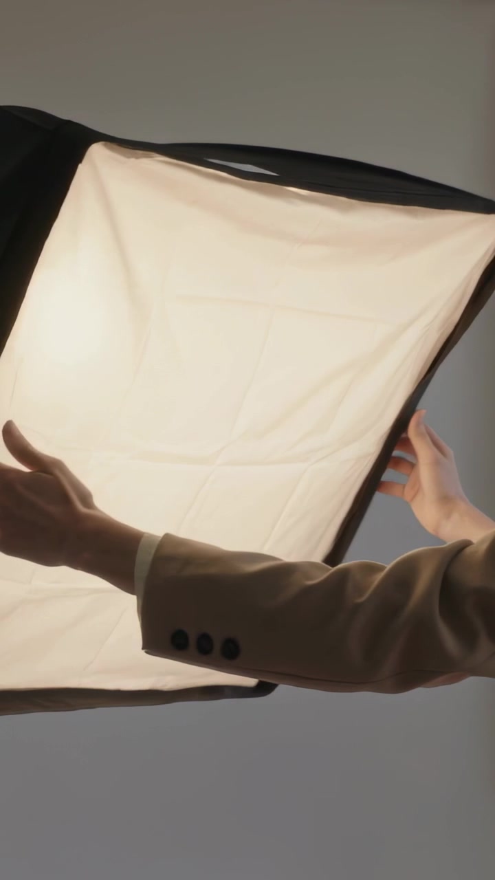 Vídeo vertical: Mulher andando com casaco bege ajustando painel em suporte no cenário, luz do entardecer, espaço para texto