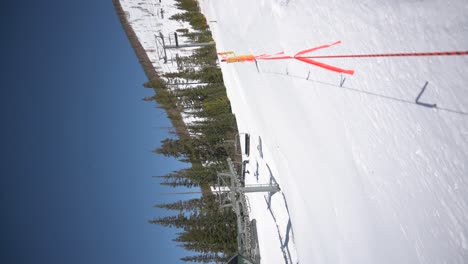 Ski-lift-carrying-skiers-and-snowboarders-up-ski-run,-vertical-timelapse