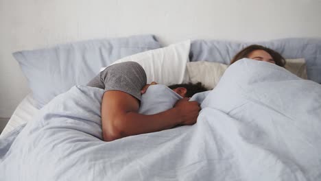 close up view of happy multiracial couple lying in bed and laughing. attractive young man and woman looking at each other with