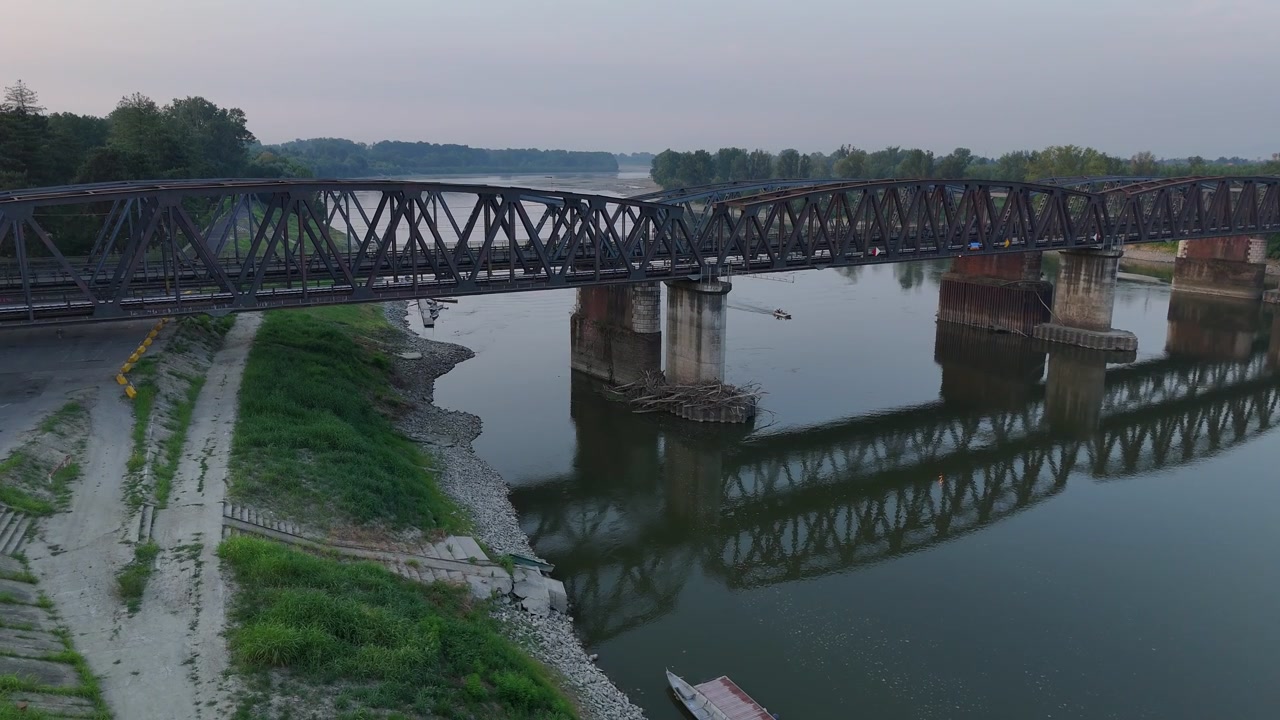 Historic steel bridge crosses the Po River between Cremona, Lombardy, and Castelvetro Piacentino, Emilia-Romagna, with exposed banks during summer 2026, low-level drone pullback.
