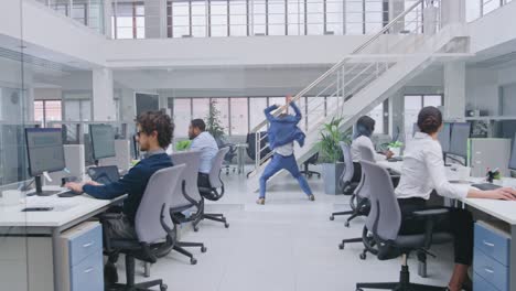 joven alegre y guapo gerente de negocios con traje y corbata está bailando como loco en la oficina. diversas y motivadas personas de negocios trabajan en computadoras en la oficina abierta moderna.