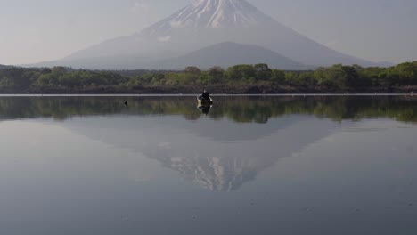 calm rivers of mount fuji with fisherman in boat catching fish, tilt up extreme wide shot