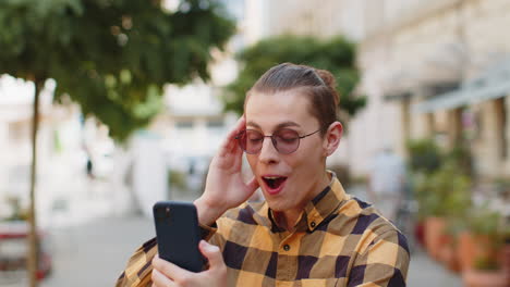 young man surprised and smiling while looking at his phone in the street.