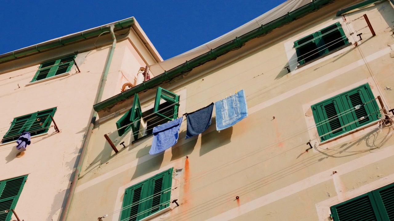 Facciata colorata di un edificio con persiane verdi e bucato steso ad asciugare su stendibiancheria all'esterno.