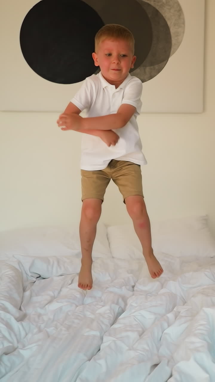 아기 소년은 현대적인 침실에서 밝은 색의 은 침대에 뛰어들고, 남성은 일시적인 비행에서 긍정적인 감정을 얻는 재미를 느니다.