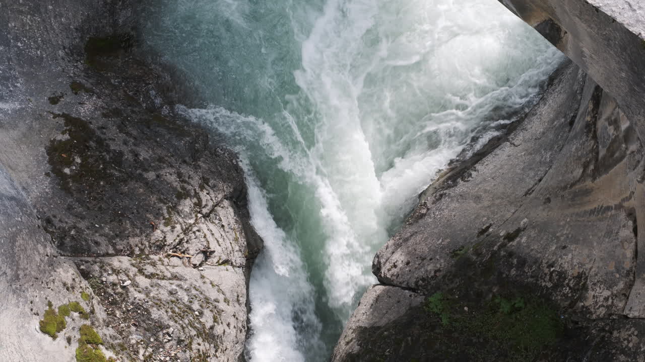 Turbulent, glacial-blue water churns and foams as it surges through a narrow, rocky gorge