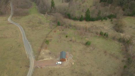 An-isolated-construction-site-with-a-newly-built-grey-roofed-structure-is-connected-by-a-winding-road-amidst-barren-trees-and-patches-of-greenery