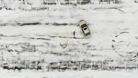 white car attempting to do doughnuts in snowy parking lot