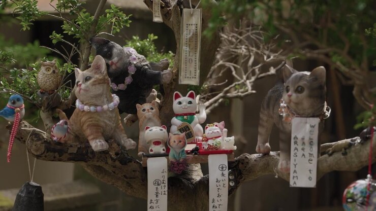 Statuette di gatti e gufi con portafortuna maneki neko su un albero ad Arashiyama, Kyoto