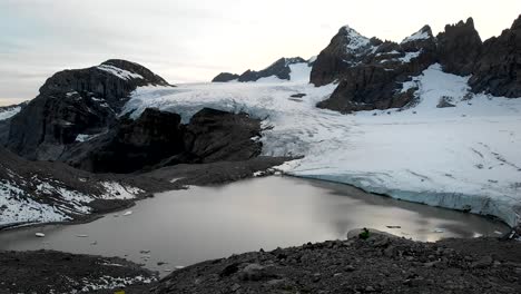 sobrevuelo aéreo sobre un excursionista disfrutando de la vista del lago glacial del glaciar claridenfirn en uri, suiza al anochecer con el cielo brillante detrás de los picos alpinos y los icebergs flotantes en el agua