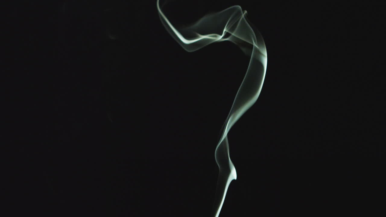 흑색 배경에 대한 프레임을 가로질러 떠다니는 불 또는 향의  연기가 가까이 올라갑니다.