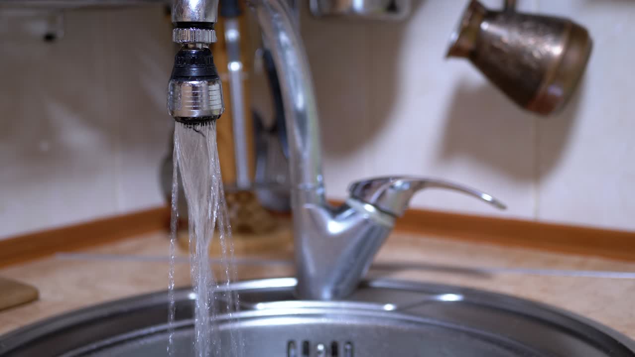 el agua de un grifo abierto recubierto de níquel fluye hacia el fregadero en una cocina moderna