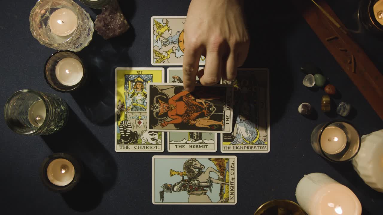 toma aérea de una persona que hace una lectura de cartas del tarot colocando cartas en la mesa con velas y cristales 4