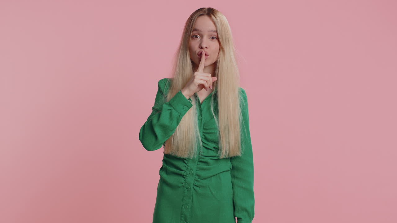 Young woman girl presses finger to lips makes silence gesture sign do not tells secret stop gossip