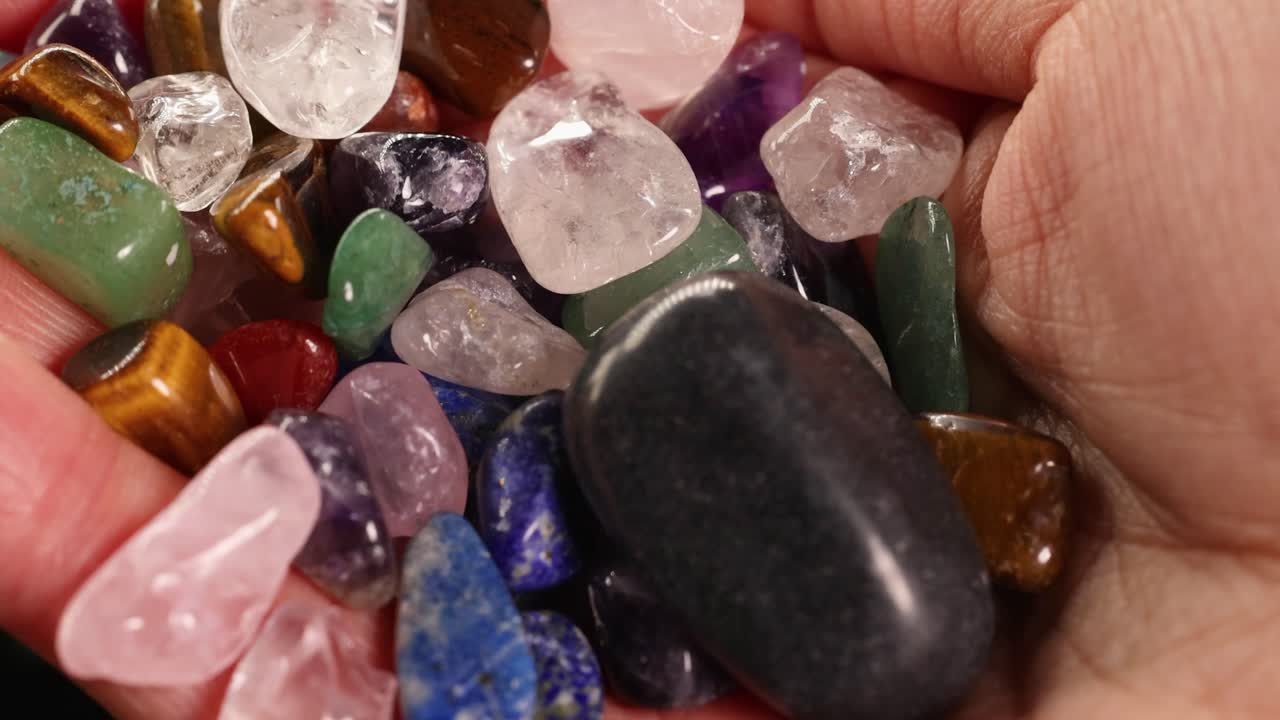 Close-up view of hands holding various chakra stones, including amethyst and tiger's eye, under warm lighting