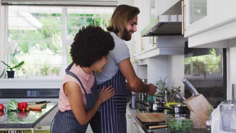pareja de raza mixta usando delantales cocinando comida juntos en la cocina en casa