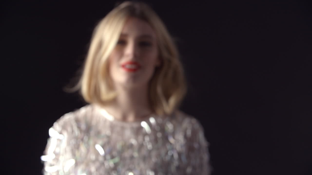 미소 짓는 화려한 금발 여성이 카메라로 걸어서 초점을 맞추고 있습니다.