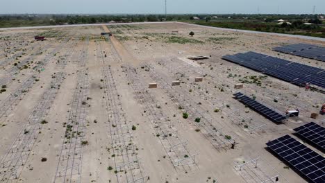 Sitio-Del-Proyecto-De-La-Planta-De-Energía-Solar-Fotovoltaica-De-Jambur-En-Construcción-Panorama-Aéreo-Izquierdo-Que-Revela-Vastas-Tierras-Y-Equipos-Vacíos-Y-Polvorientos