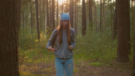 female hiker with backpack walks through peaceful forest, adjusting her bag while bathed in soft evening sunlight, her contemplative expression