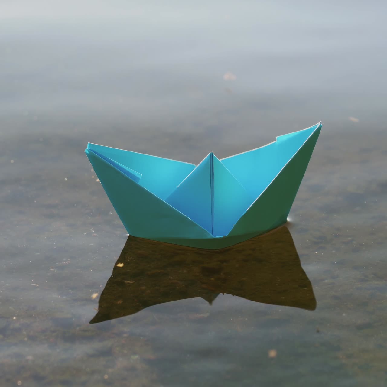 Blue paper boat sailing on water on romantic sunset. Origami.
