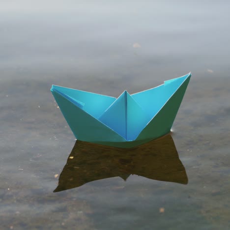 blauwe papieren boot die op het water zeilt bij een romantische zonsondergang. origami.
