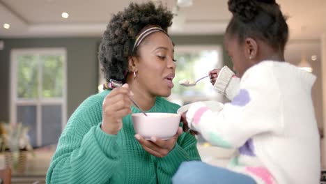 african american mother and daughter eating cereal with milk in kitchen, slow motion
