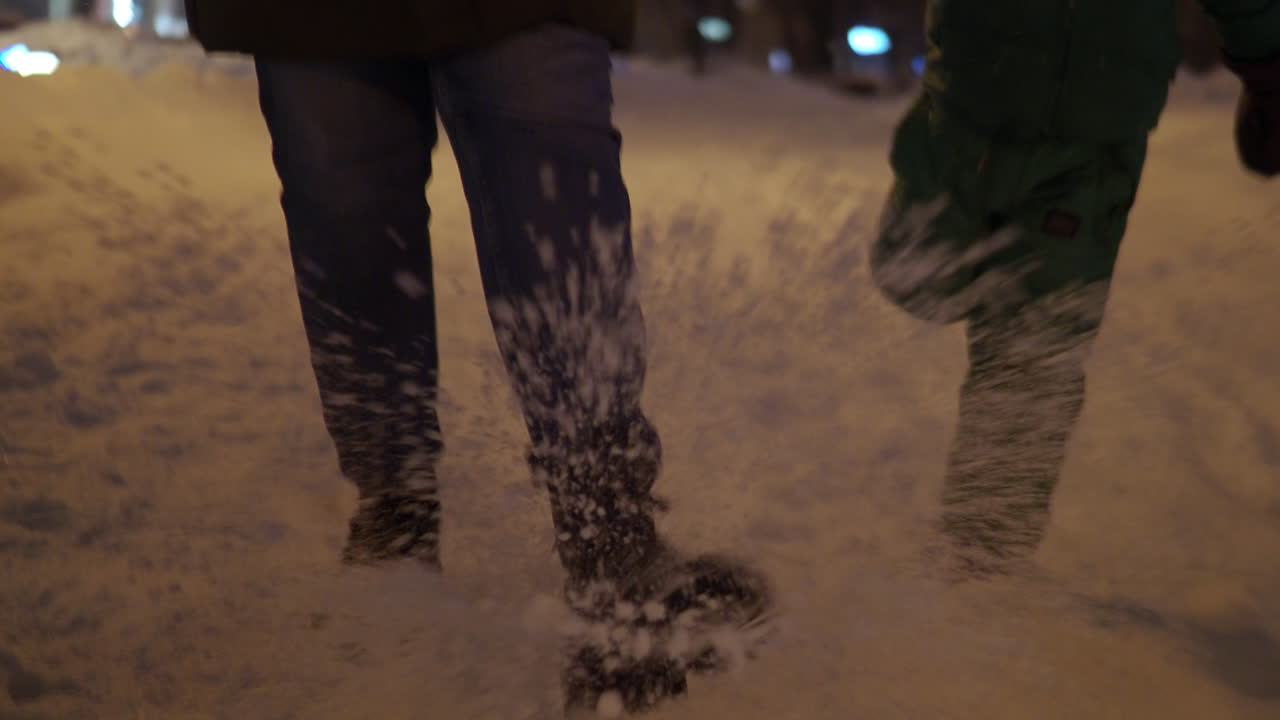 Mum and daughter kicking snow on the sidewalk