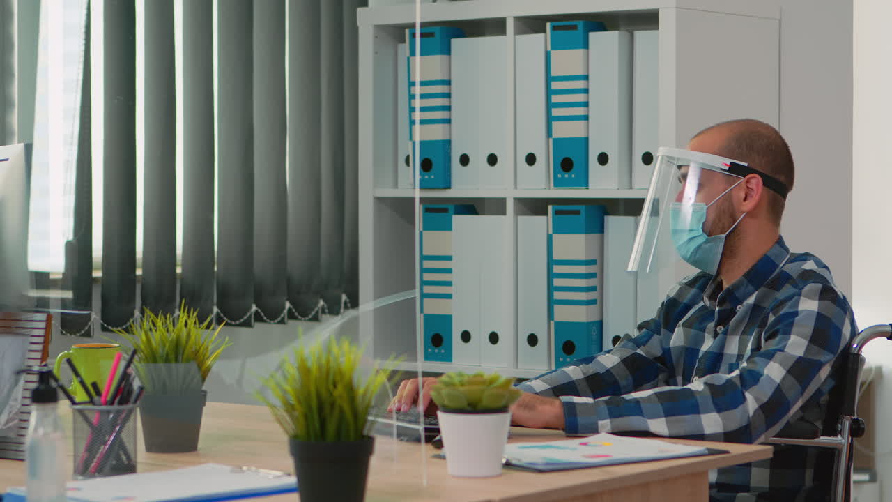 Empresario paralizado con mascarilla escribiendo en la computadora