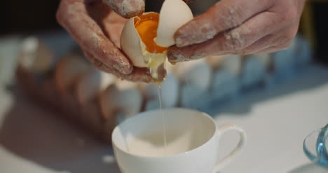 woman breaking egg into bowl in kitchen