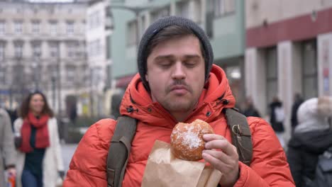 man eating traditional polish donut on city street